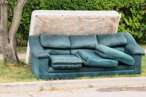 A discarded blue couch sitting outside against a wall